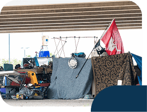 Makeshift shelter under highway overpass with flag.