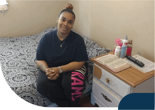 Person seated next to bed and nightstand with book.