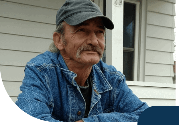 Man in denim jacket and cap on porch.