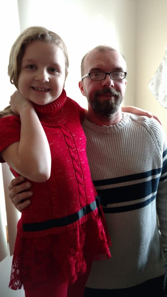 Child in red outfit with adult indoors smiling.
