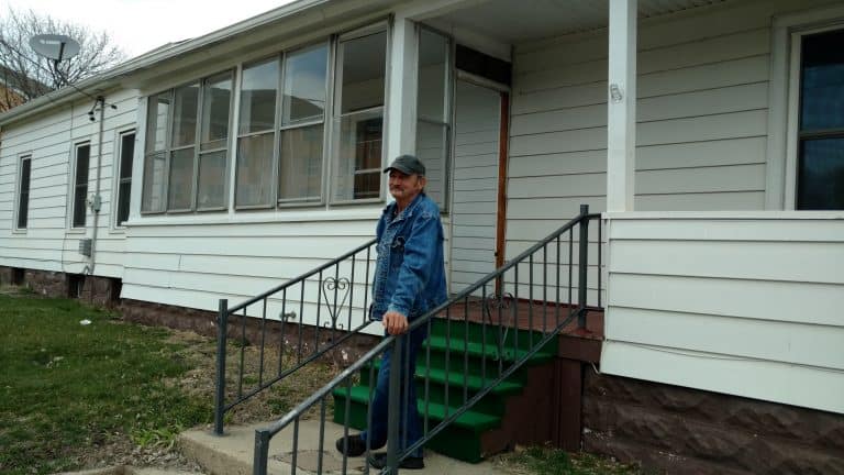 Man standing on porch of white house.