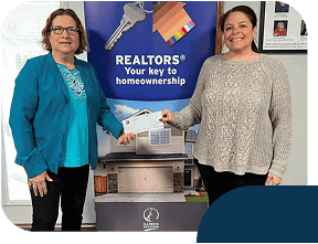 Two women with Realtor sign holding check