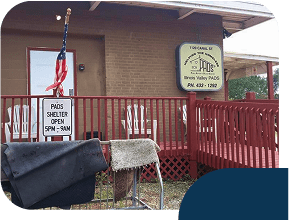 Homeless shelter entrance with flag and open hours sign.