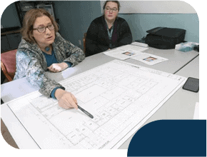 Two people discussing architectural blueprint at table.